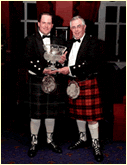 Two men in kilts holding a trophy