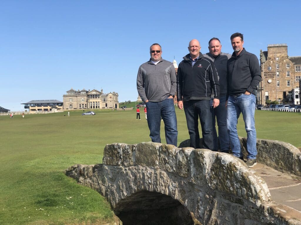 Four men standing on a rock near a stone bridge.