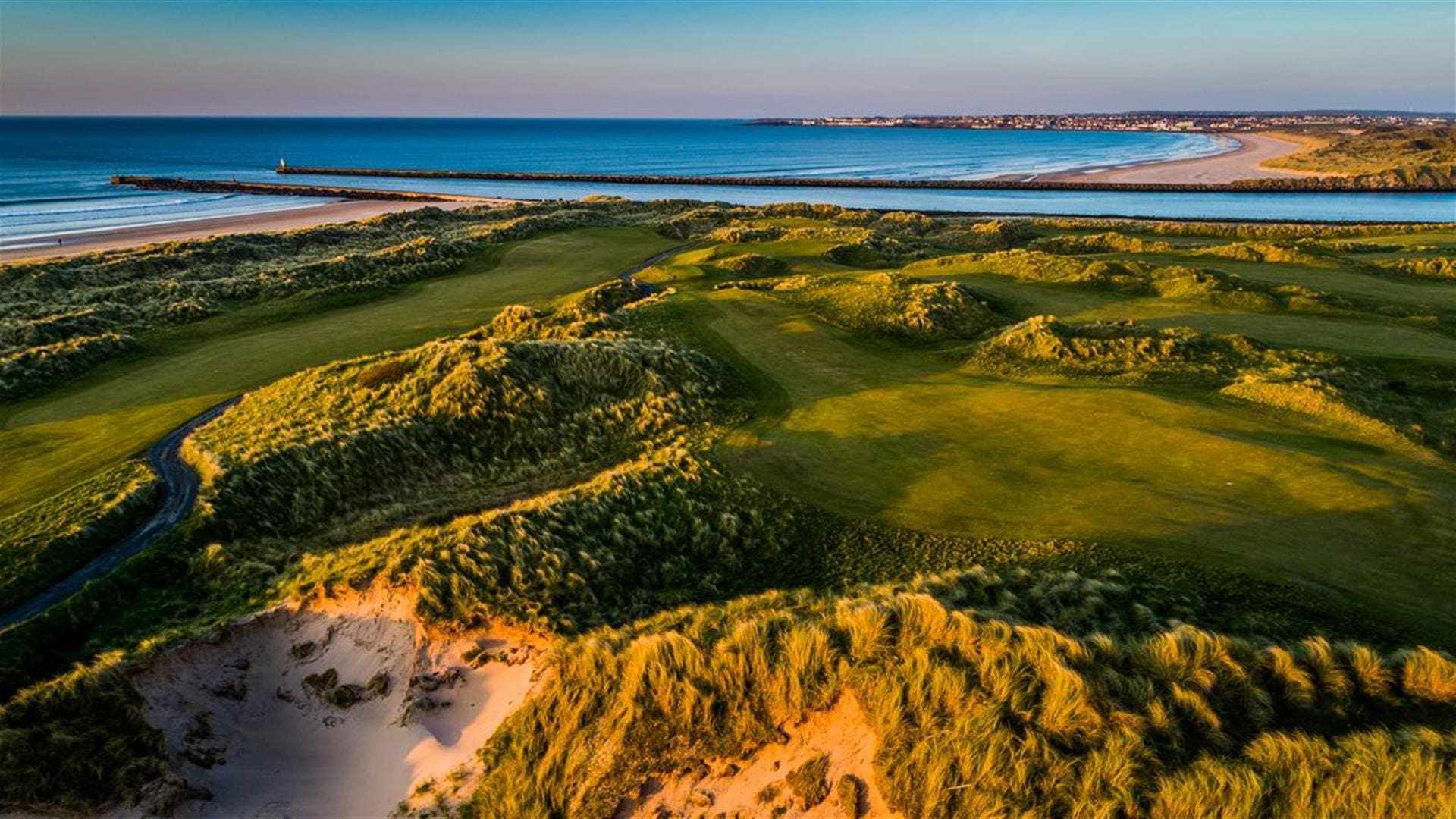 A view of the ocean from above, with sand dunes and grass.