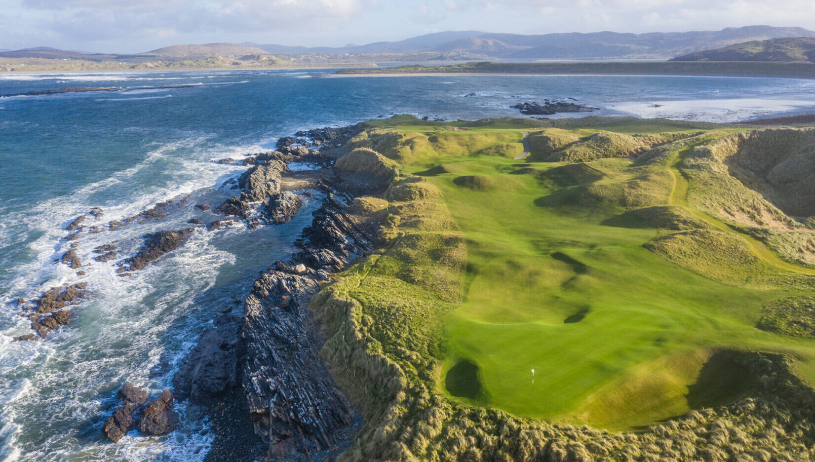 A view of the ocean from above shows a green golf course.